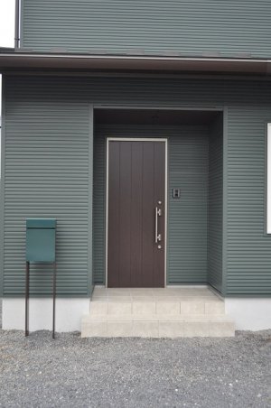 カーキ色の外壁とシンプルデザインの玄関ドア